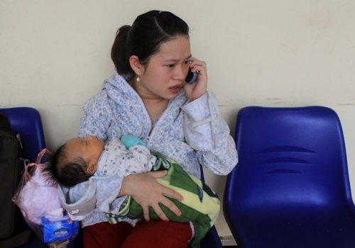 Chị Trần Thị Phượng một tay đang bồng con, tay đang nghe tin tức của chồng về bệnh tình của cháu Tài tại Bệnh viện Nhi Trung ương. 
