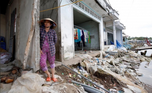 Một phụ nữ đứng bên ngôi nhà ven sông bị hư hỏng nặng do lở đất tại Cần Thơ (Ảnh: Kham/Reuters)